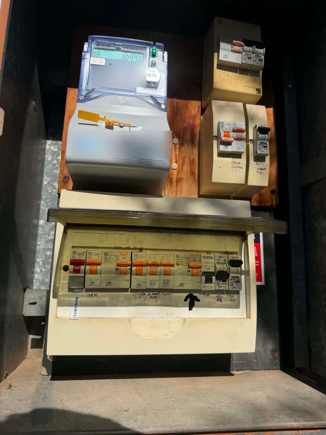 The same full switchboard seen wider, showing the meter and the dark backing panel it's all mounted on