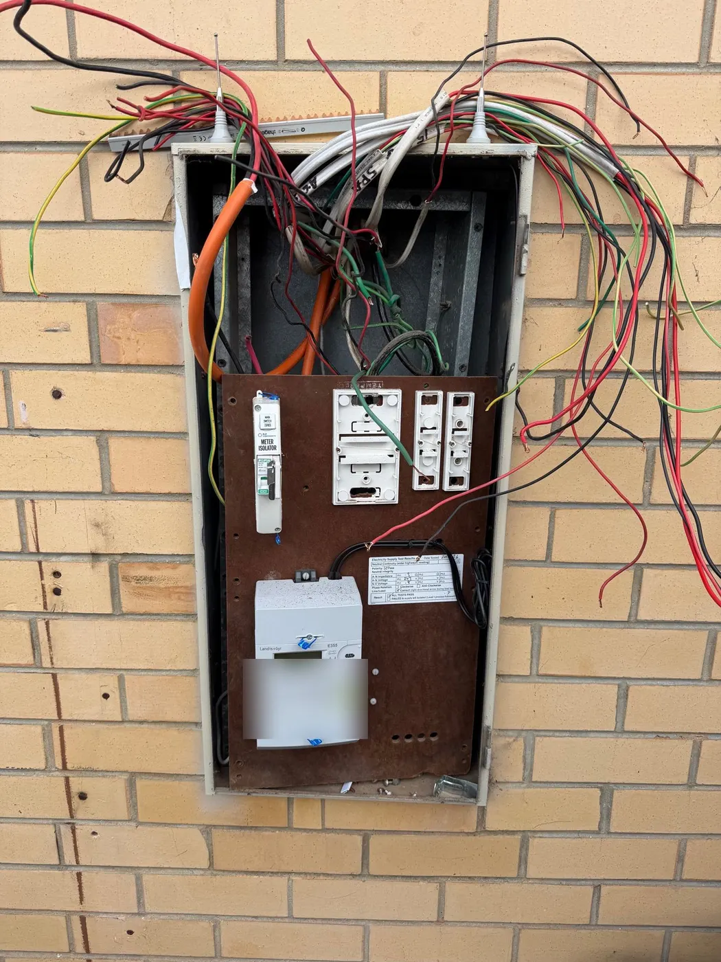 Switchboard enclosure stripped back with circuits hanging loose and the brown asbestos backing panel exposed