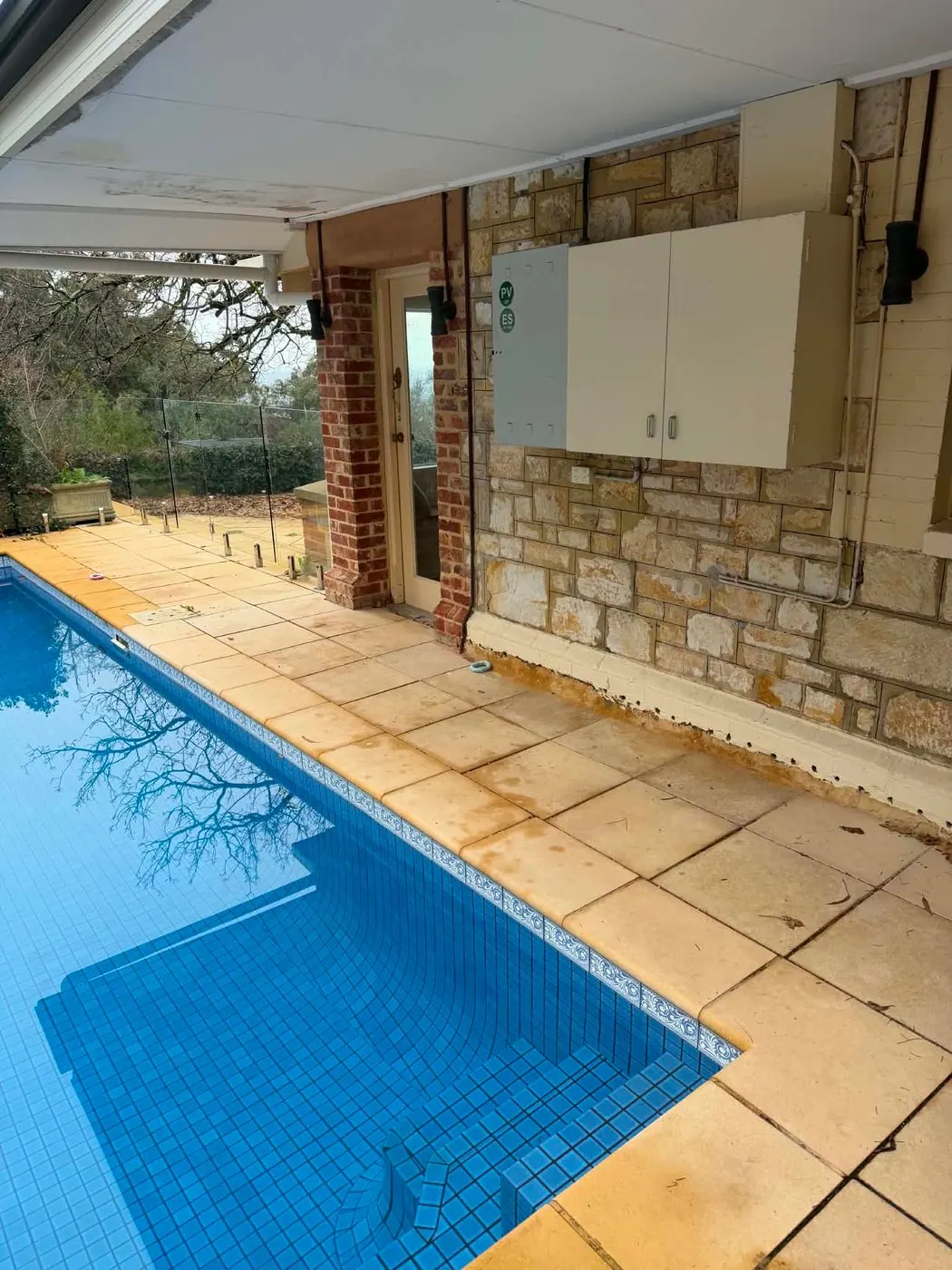 Switchboard cabinet mounted on a wall directly beside a swimming pool